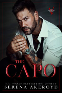 A rugged looking man in his 30s with dark brown hair and a beard. He is wearing a white dress shirt that is unbuttoned at the top with his bow tie untied. His sleeves are rolled up to reveal colorful tattoos and his watch. Text reads: The Capo - USA Today Bestselling Author Serena Akeroyd